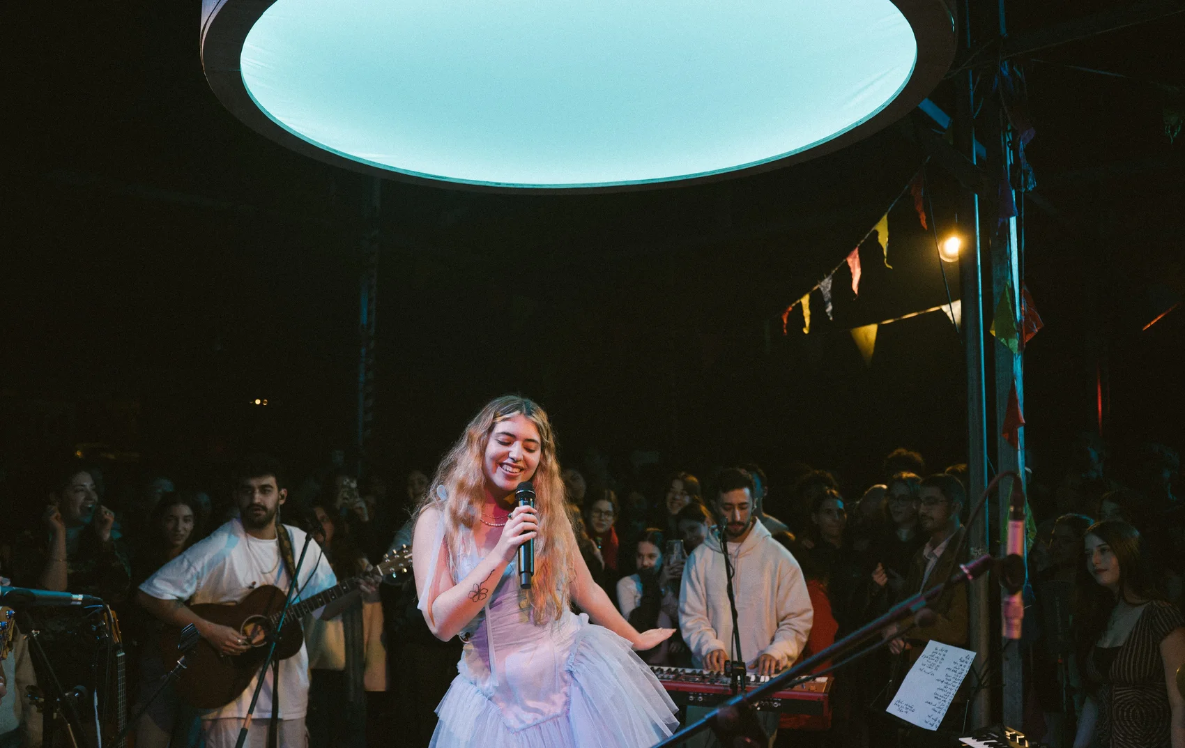 Alma Gov performing with her band beneath a large overhead light