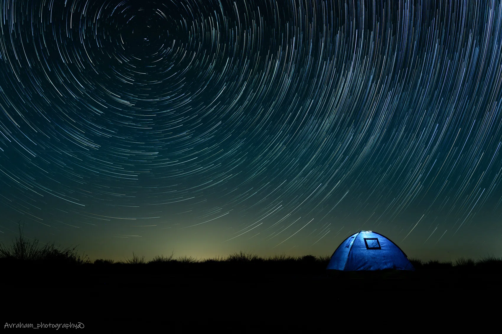 Star trails circling above an illuminated tent at night